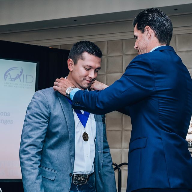 A man pulling a medal around another a fellows neck.