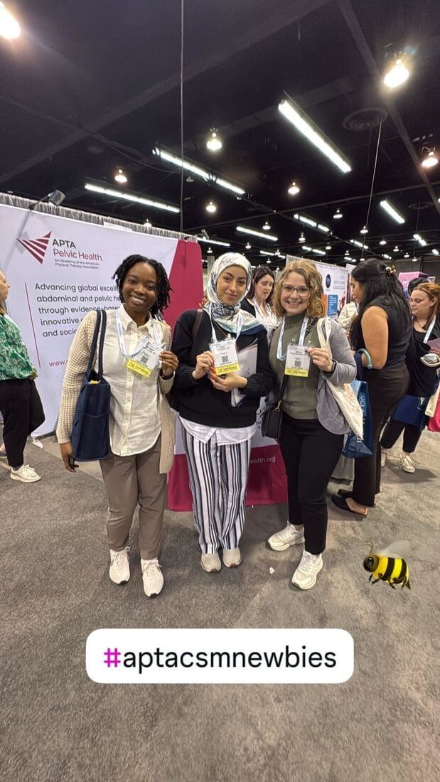 Three attendees smiling in front of the APTA Pelvic Health booth