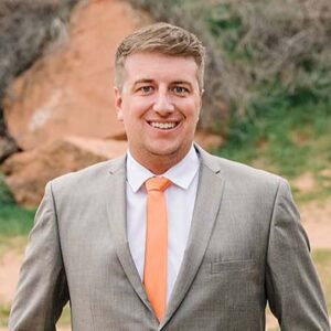 White man in a gray business suit, white shirt, and salmon tie.