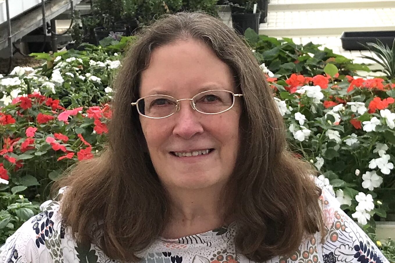 Older white woman with brown hair, glasses, and a floral patterned shirt.