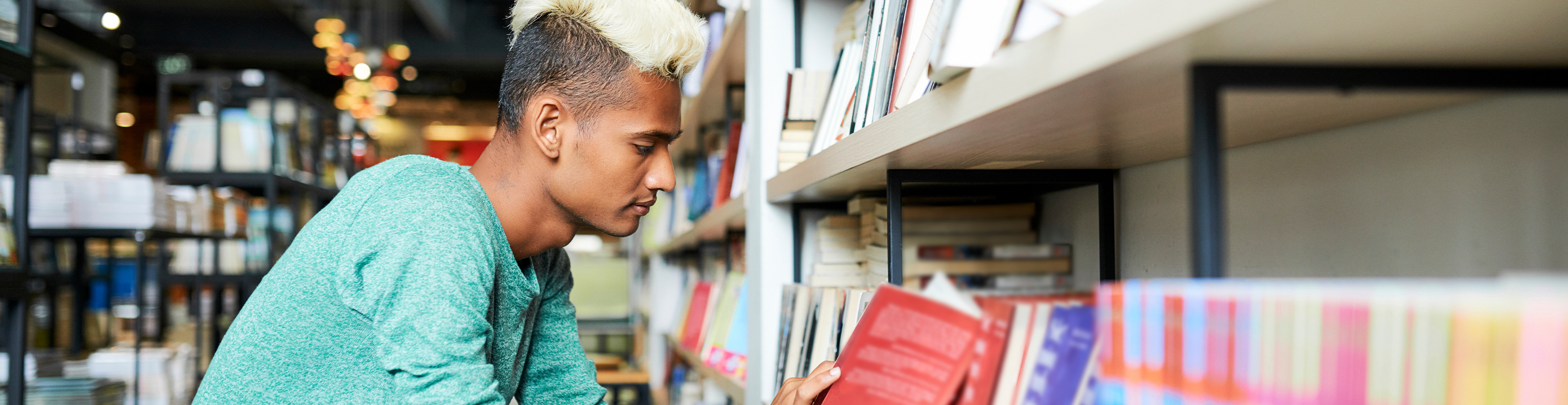 Image of a person in a bookstore environment, crouching down to a lower shelf and reading the back of a book