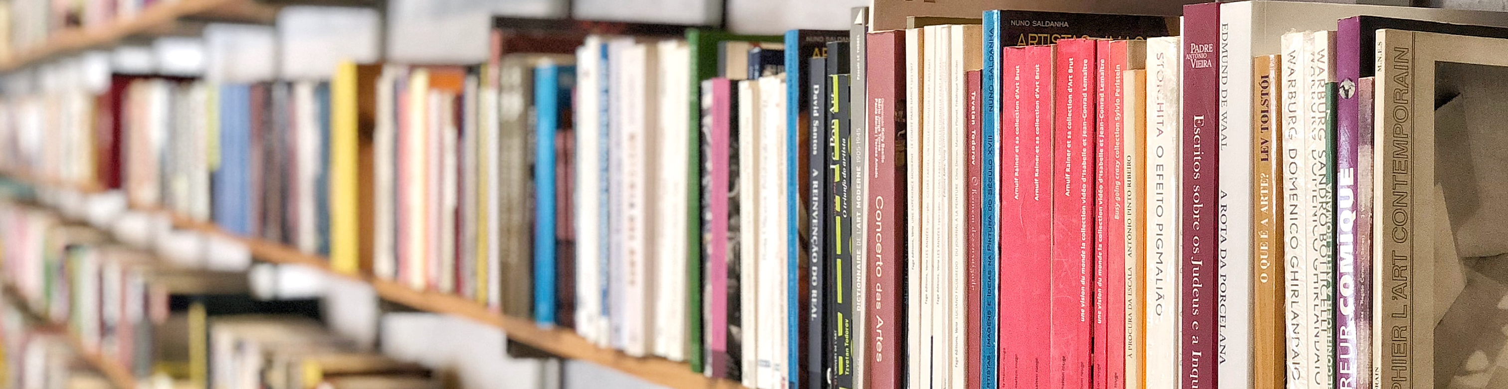 An angled close-up of a wall of light wood shelves lined with books.