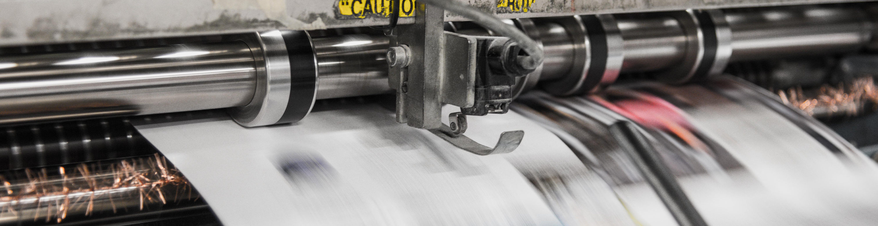 A close-up of a printing press as paper is being printed on. The paper is motion-blurred.