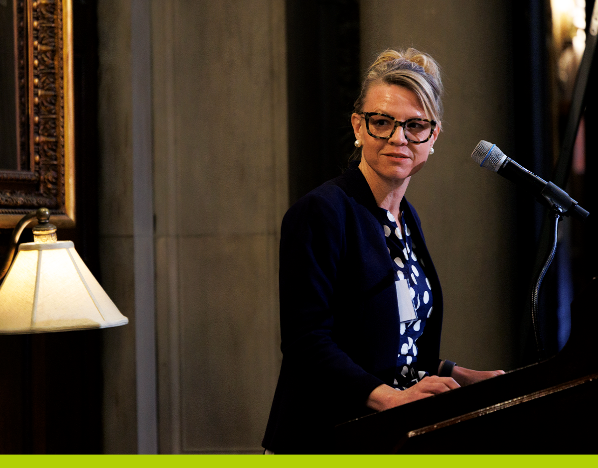 A woman standing behind a microphone at a BISG event. She is looking off-camera to a speaker beside her.