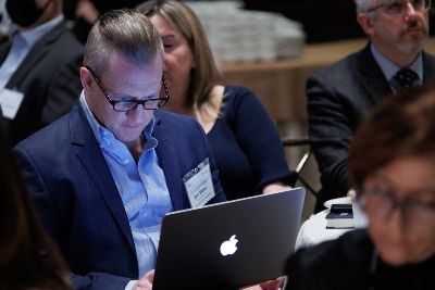 A man seated at a table at a BISG event is looking at his laptop. His face is aglow with the light from the screen. 