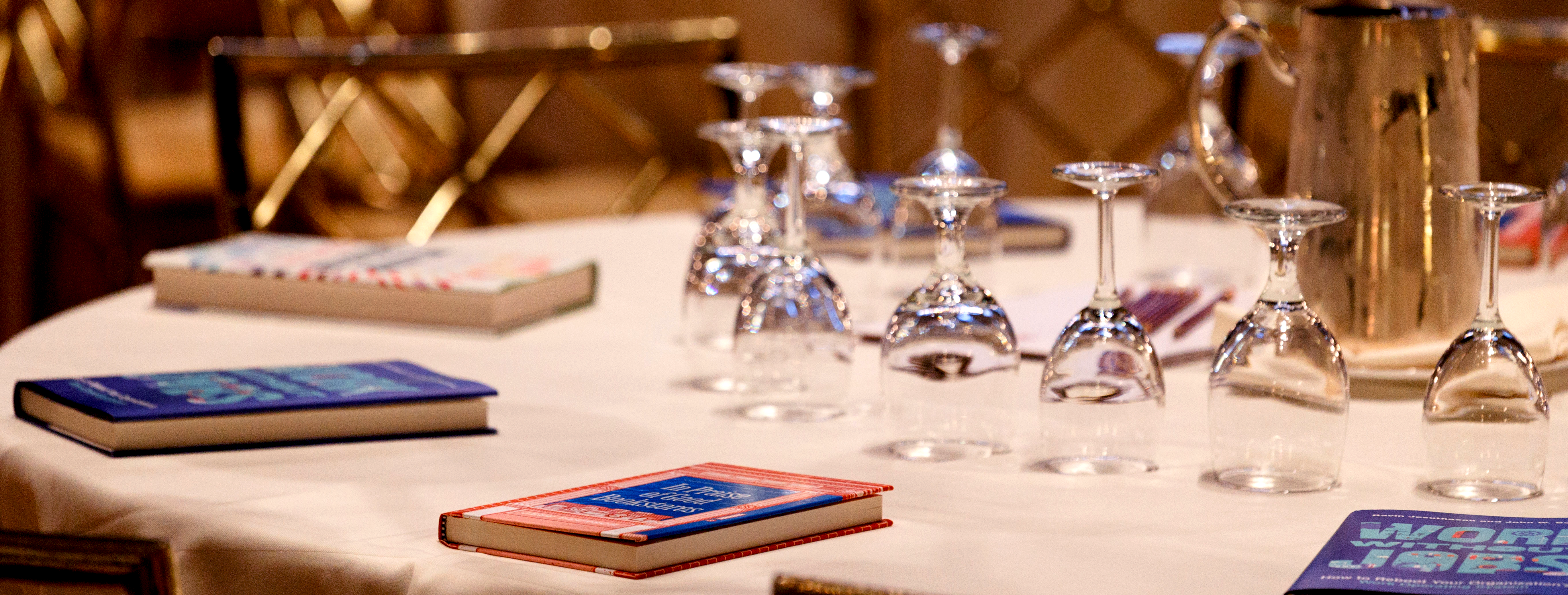 Close-up of a table at a BISG event pre-event. The table is set with wineglasses, a pitcher, and an array of books.