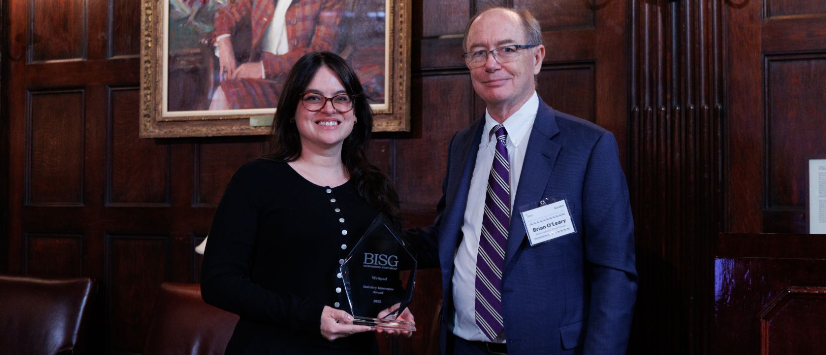 A man and a woman at a BISG event. The woman is holding an award labelled 