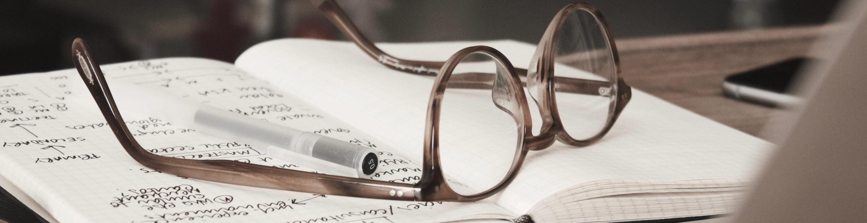 A pair of glasses set down atop a notebook with handwriting in black ink.
