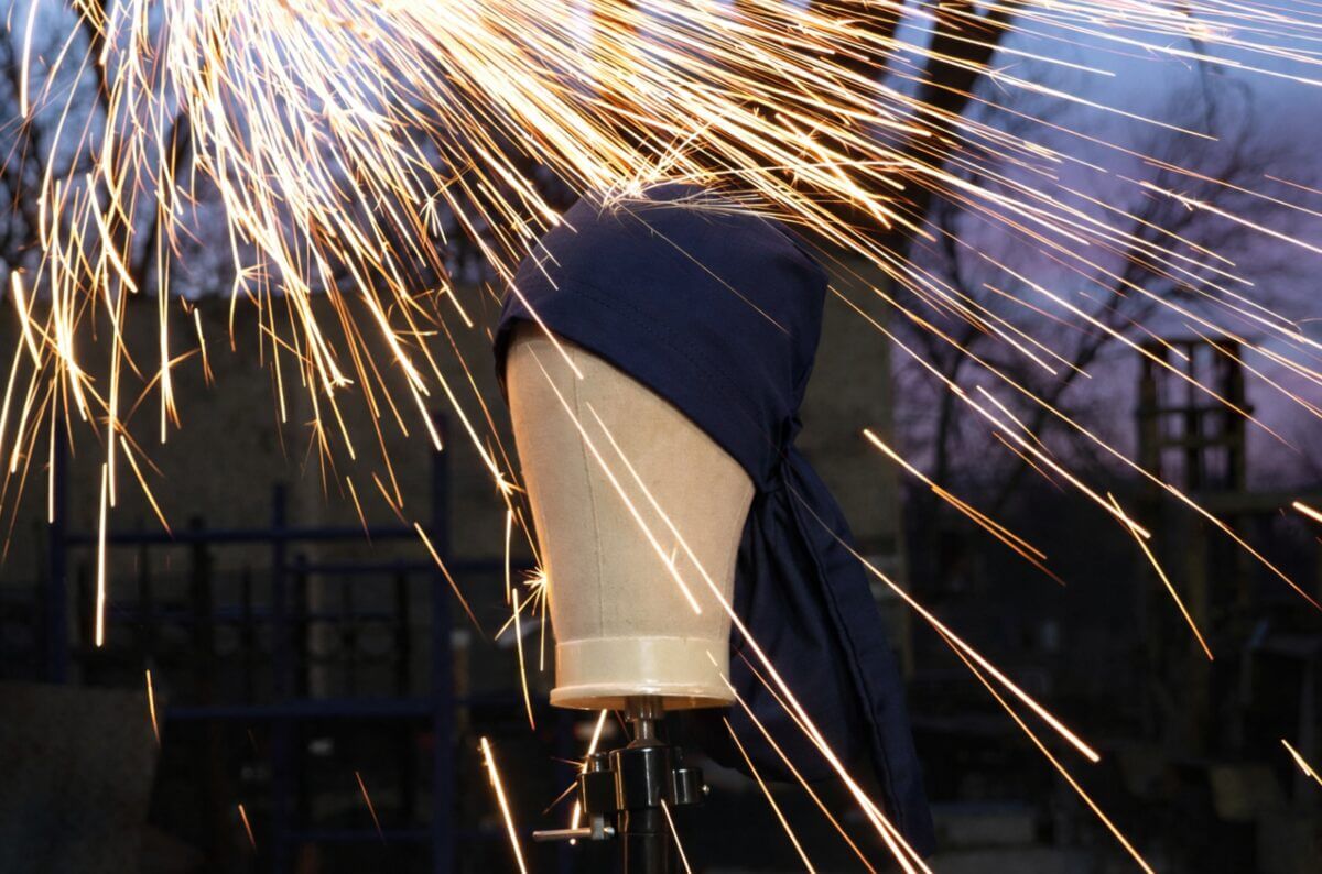 A navy SparkDefy welding cap on a mannequin head with welding sparks flying across it
