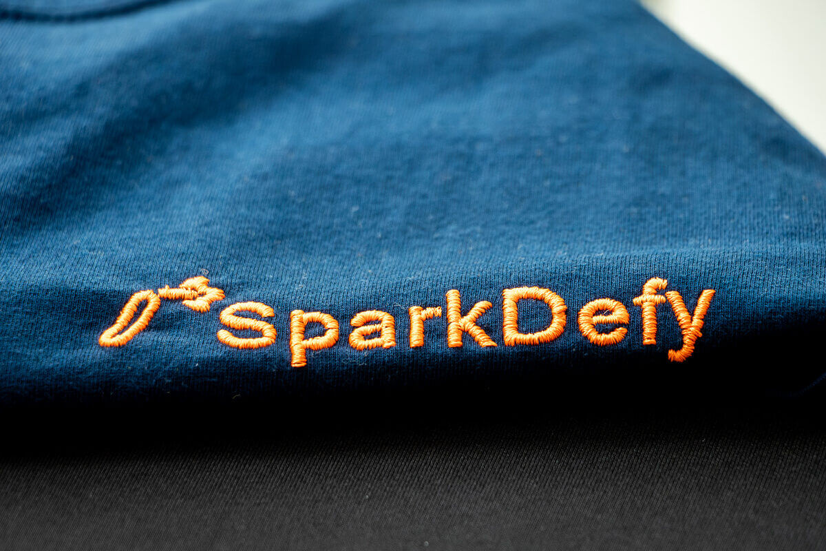 The SparkDefy logo embroidered in orange thread on navy fire-resistant fabric