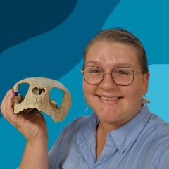 female, light hair and glasses, white, smiling at the camera holding a fossil