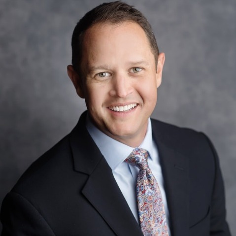 The image depicts a well-dressed individual in a black suit and tie, wearing a patterned handkerchief.AI-generated content may be incorrect.