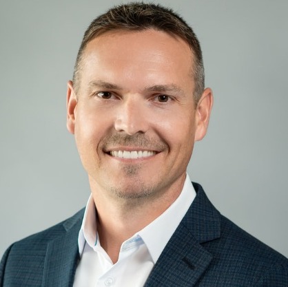 The image shows a person dressed in a blue suit with a white dress shirt, wearing a red tie.AI-generated content may be incorrect.