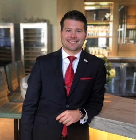 A well-dressed individual in a bar, holding a wine glass, standing next to a modern bar counter.AI-generated content may be incorrect.