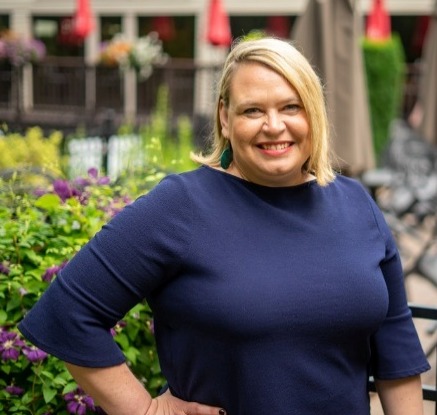 The image shows a person standing outside, wearing a dark blue shirt, with a beautifully decorated garden and red umbrella in the background.AI-generated content may be incorrect.