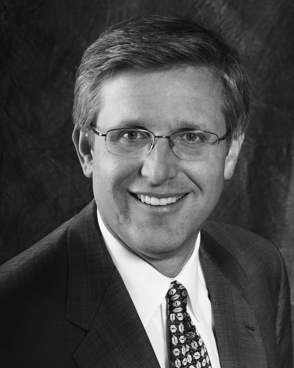 Black and white headshot of program presenter, Scott Mietchen, wearing a suit