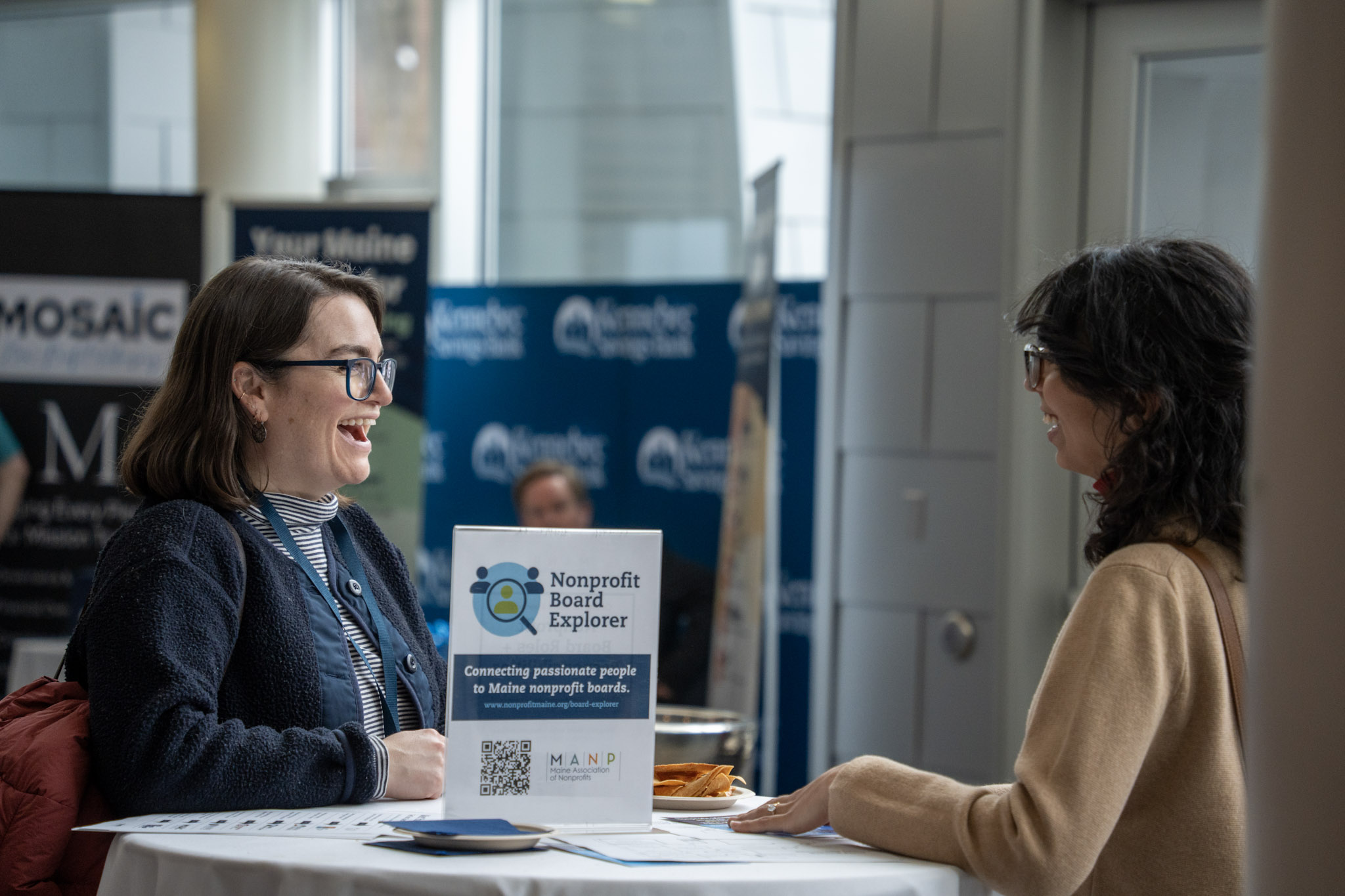 Two event participants standing at a table engaged in conversation and smiling.