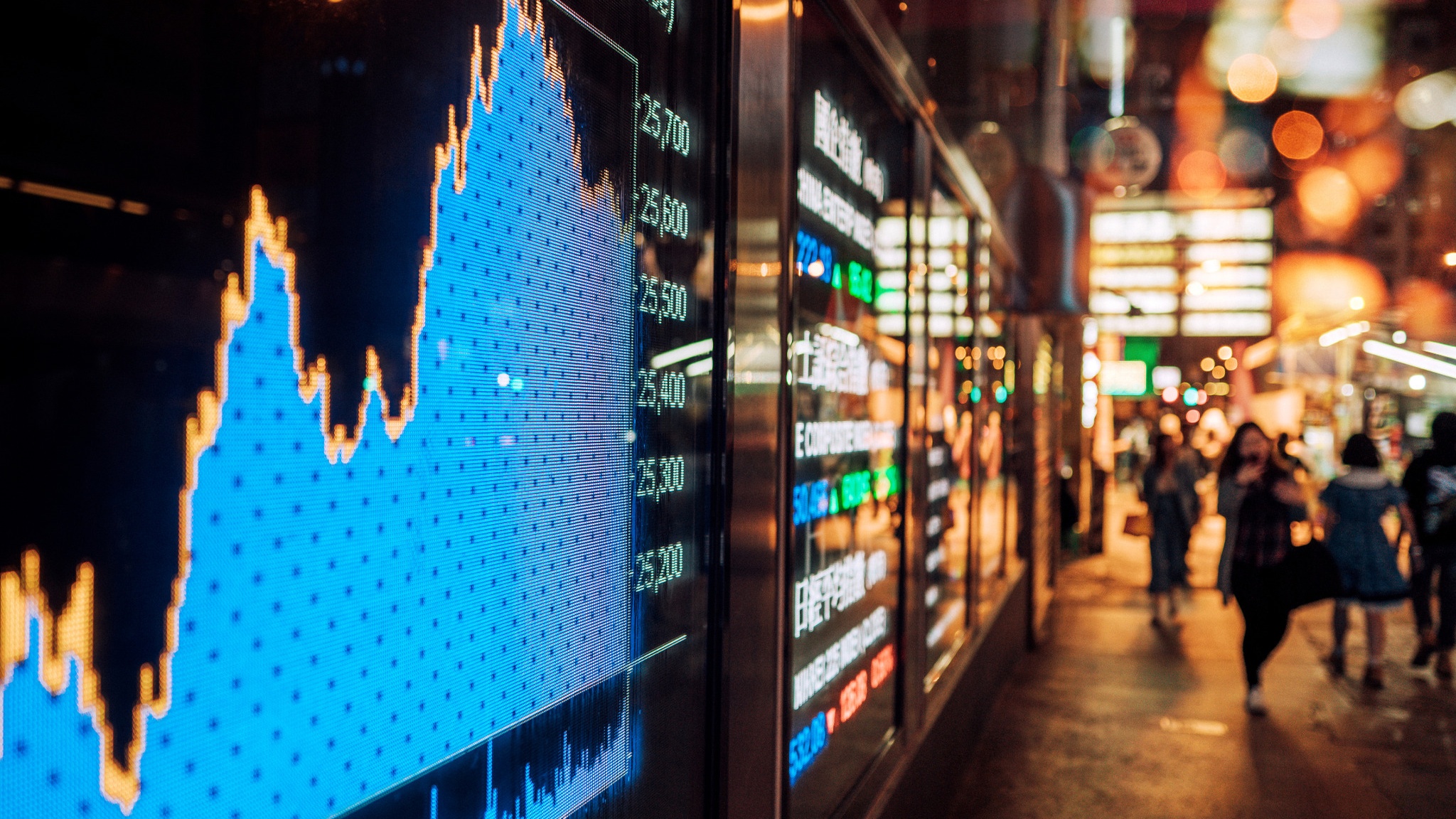 Stock market display with a bright line chart in a city setting at night.