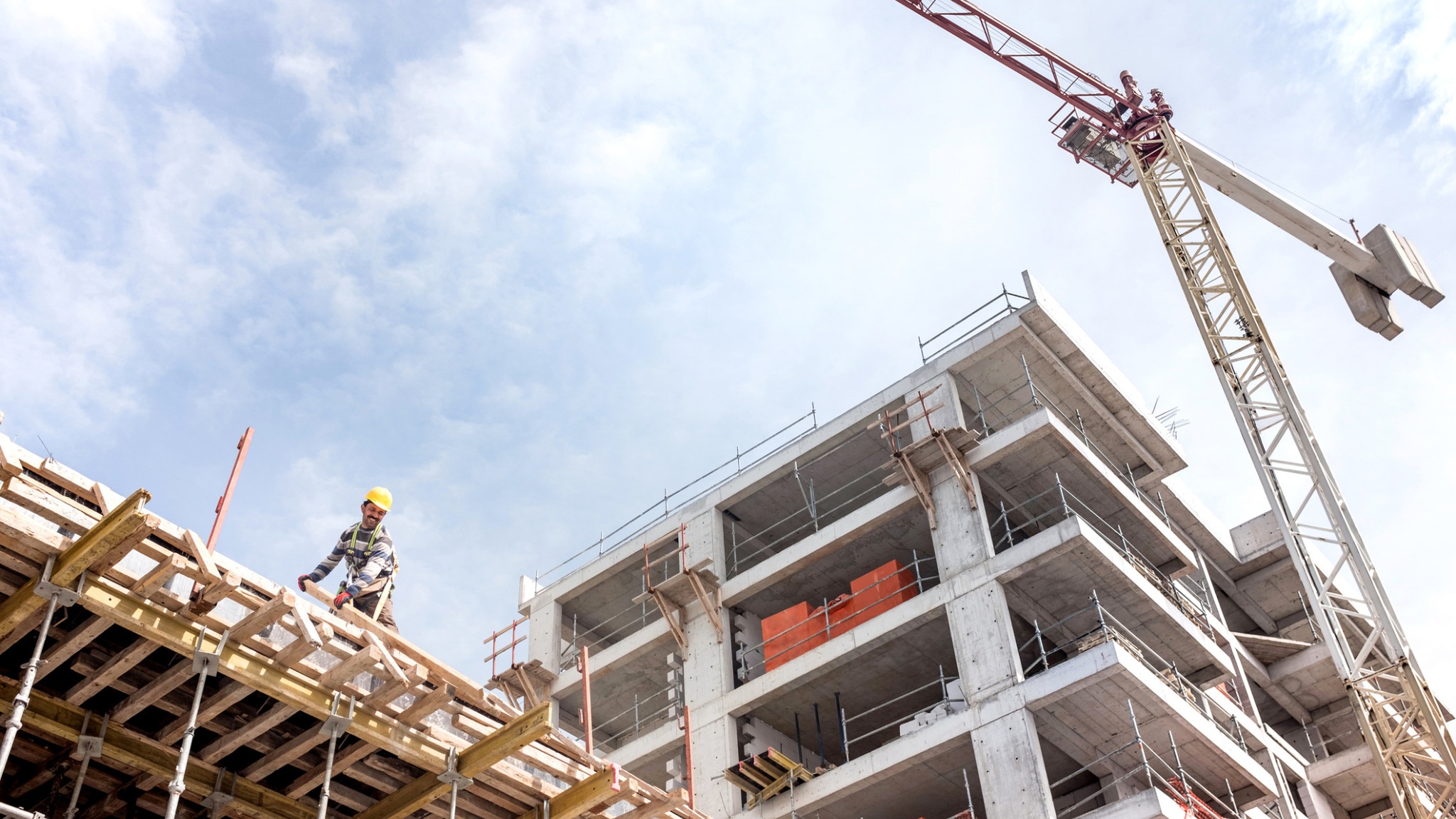 Construction workers and cranes at a large building site under a bright sky.