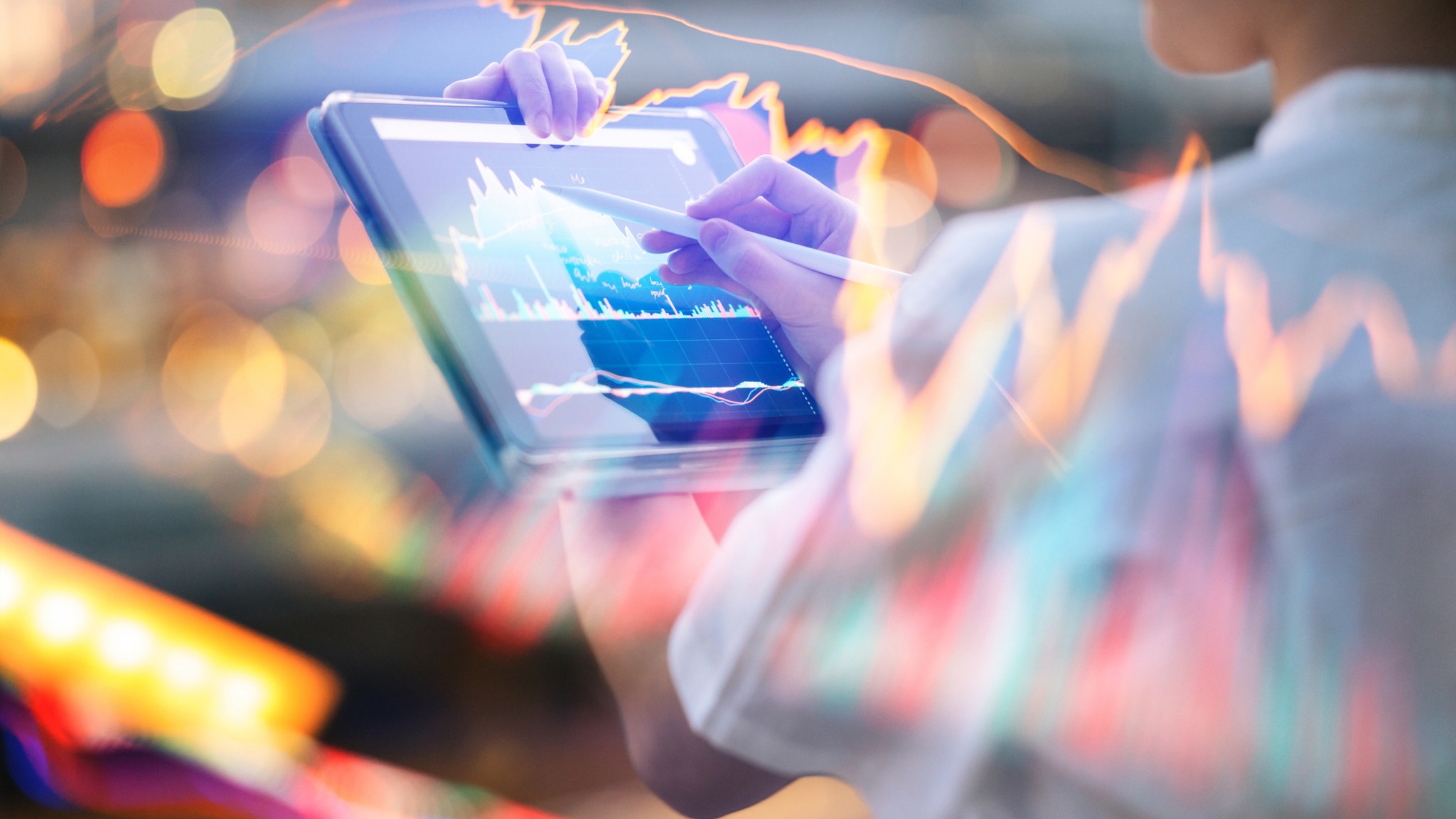 Person using a tablet with colorful market graphics and an overlaid chart.
