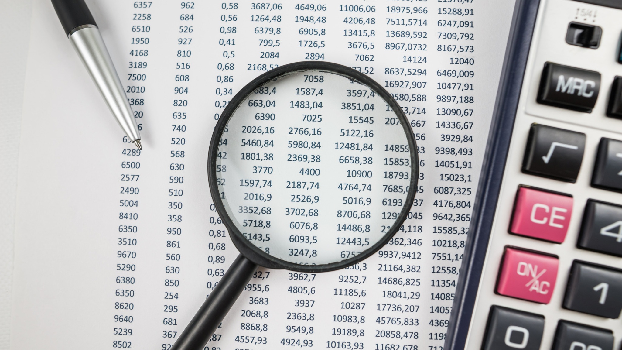 Calculator, pen, and spreadsheet with rows of numerical data.