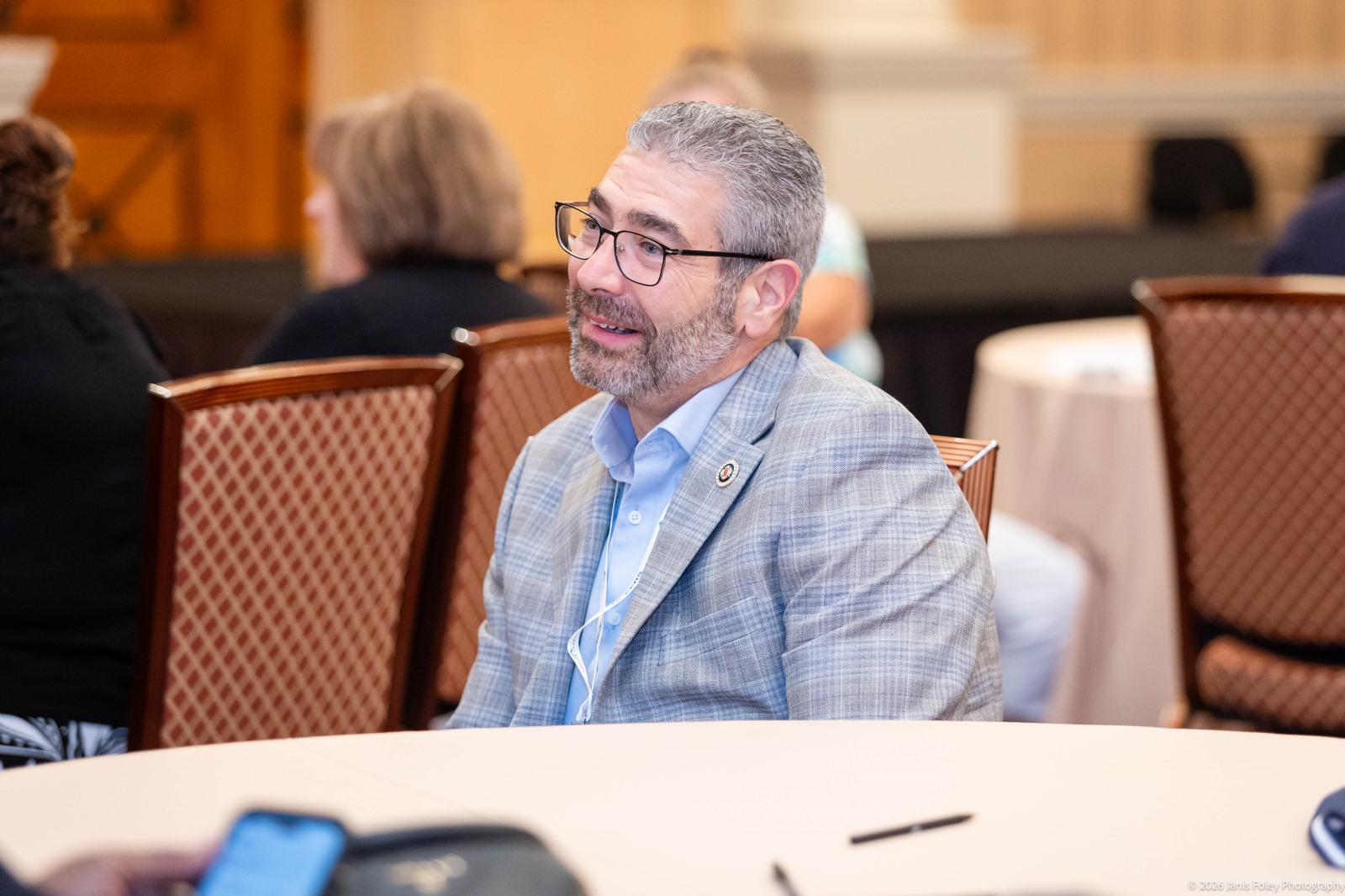 Attendee sitting at a table smiling during a presentation