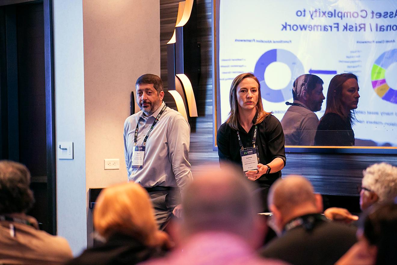 Two presenters on stage standing in front of financial graphs