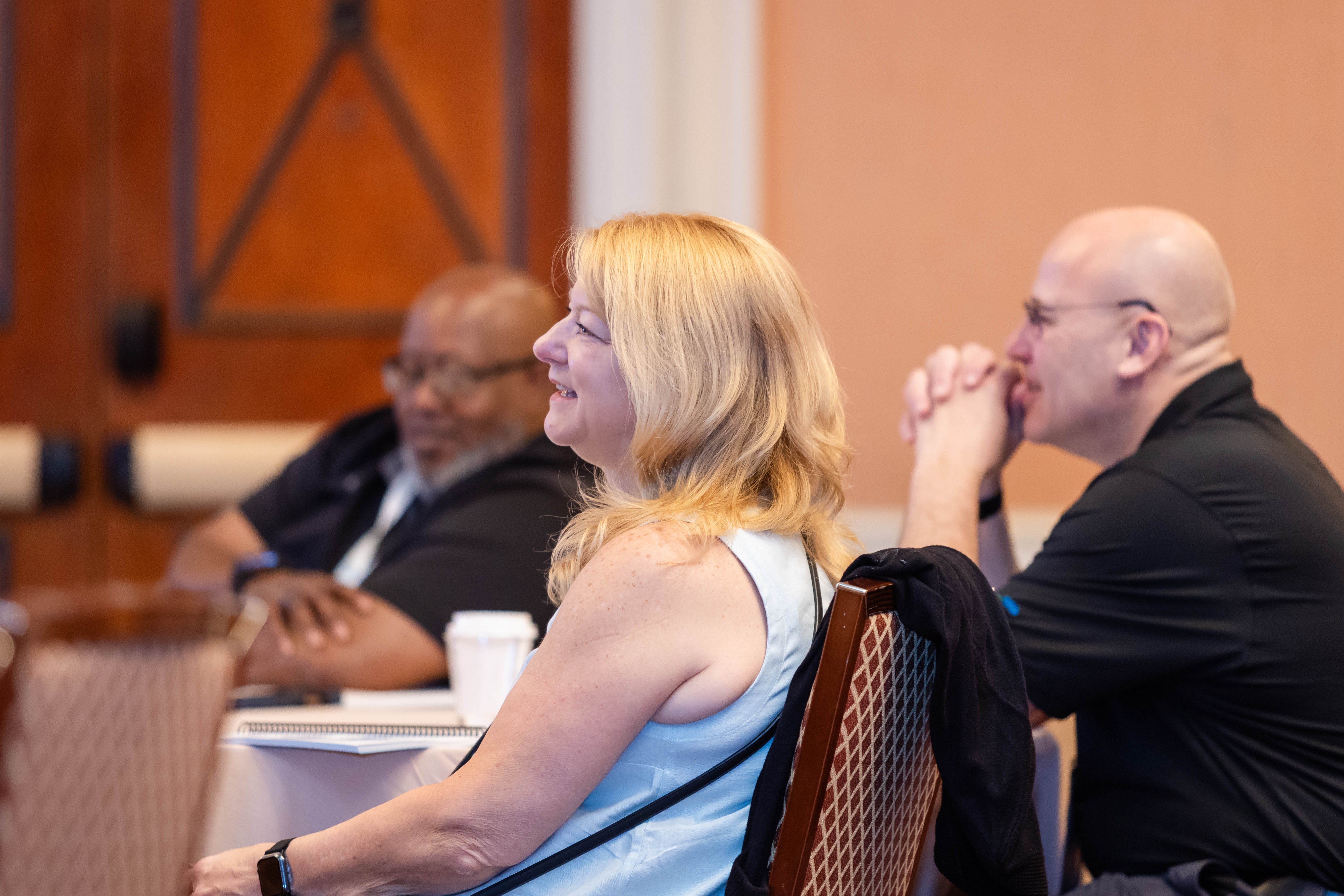 Lefthand shot of attendees in the audience smiling during a presentation