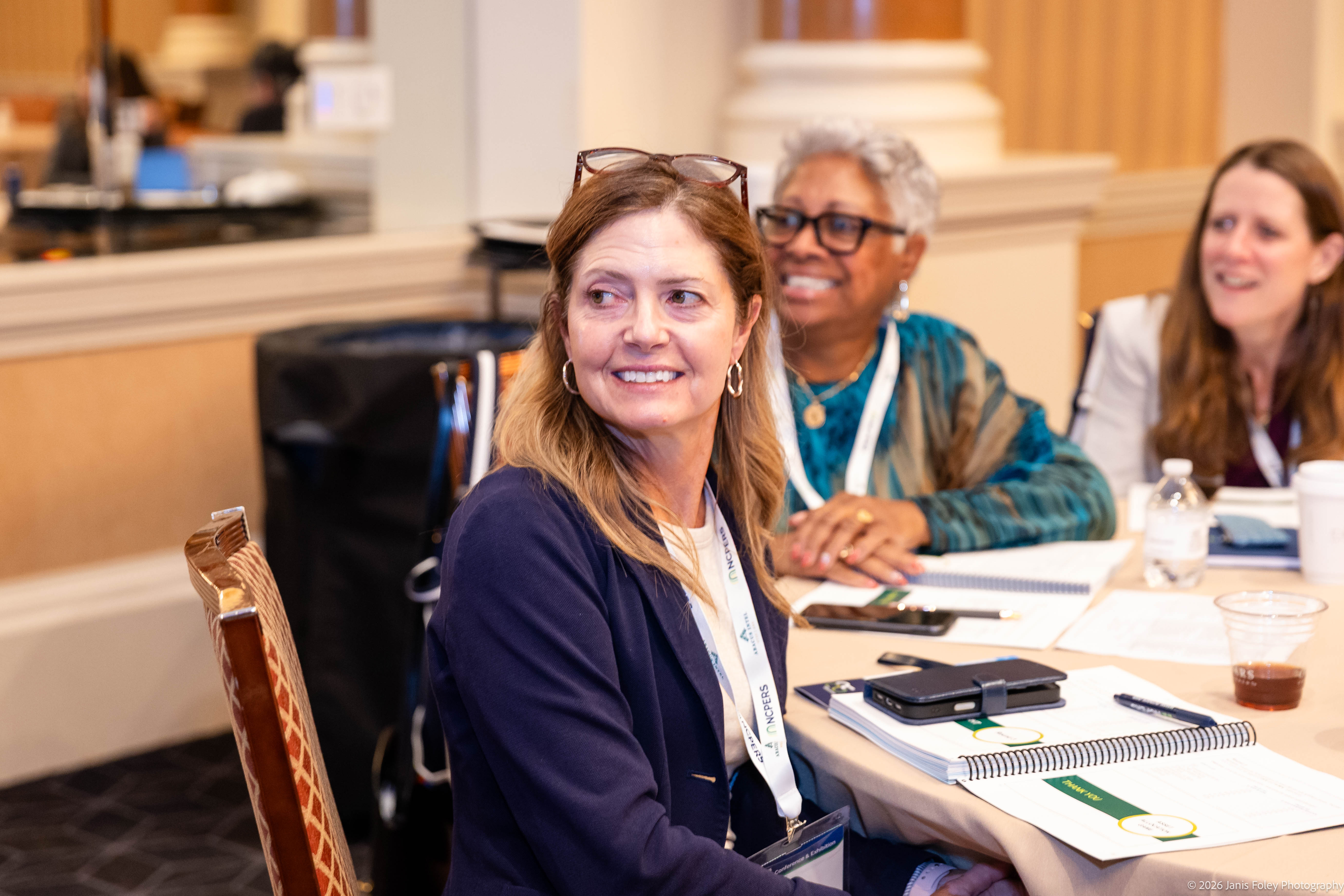 Three attendees smile with notebooks at a Trustee Essentials Training session table