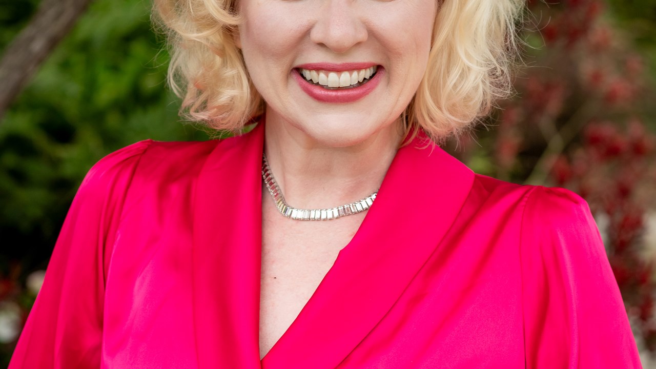 Amy in a magenta colored wrap dress smiling at the camera.