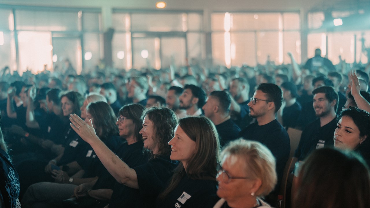 Engaged audience of 1,000+ at Gabriel Schandl's closing keynote, smiling and raising their hands.