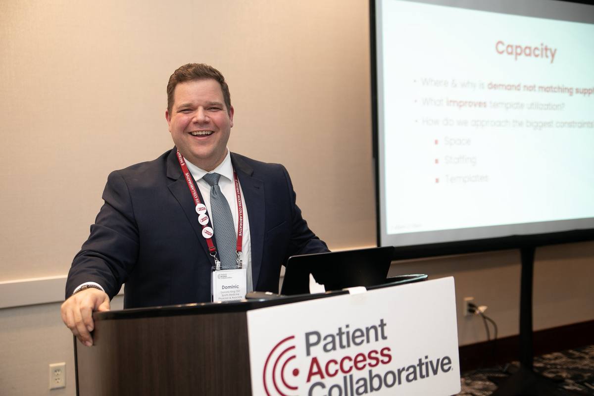 A speaker smiling at the Patient Access Collaborative podium during the 2026 Symposium