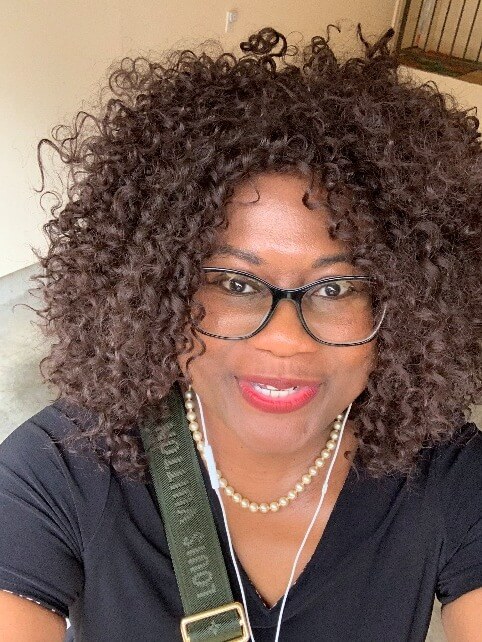 A person with curly hair wearing glasses and a necklaceAI-generated content may be incorrect.