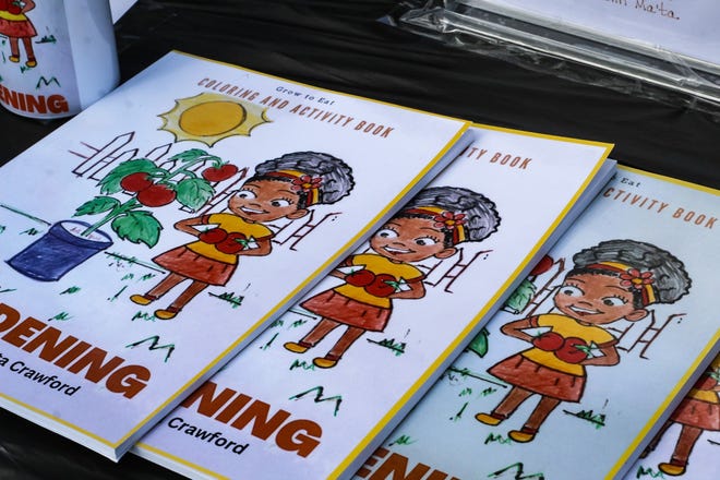 En un festival del Día de la Tierra en Unity Park, Ma'ta Crawford muestra sus libros educativos para colorear. Se inspiró para crearlos después de hacer dibujos similares para su nieto tras haber cultivado juntos un huerto cuando él era niño.