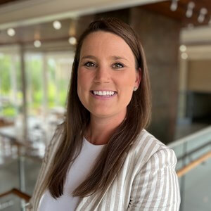 Picture of Katie Peterson, a smiling woman with brown hair, wearing a white shirt and tan and white striped blazer. 