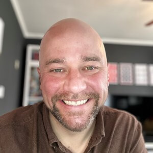 Picture of Michael Carmody, a smiling, bald, bearded man wearing a brown polo.